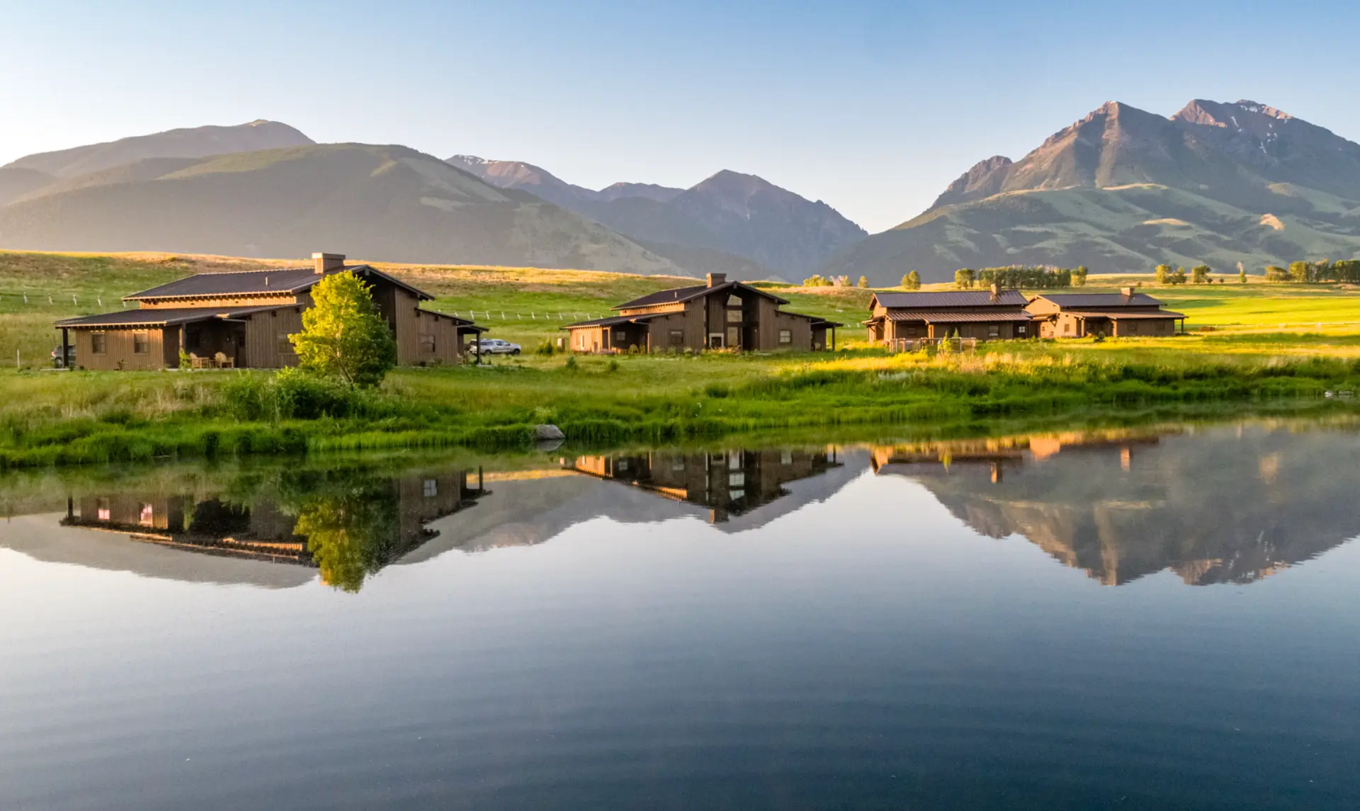 Sage Lodge ranch houses reflected in the pond beneath the mountains