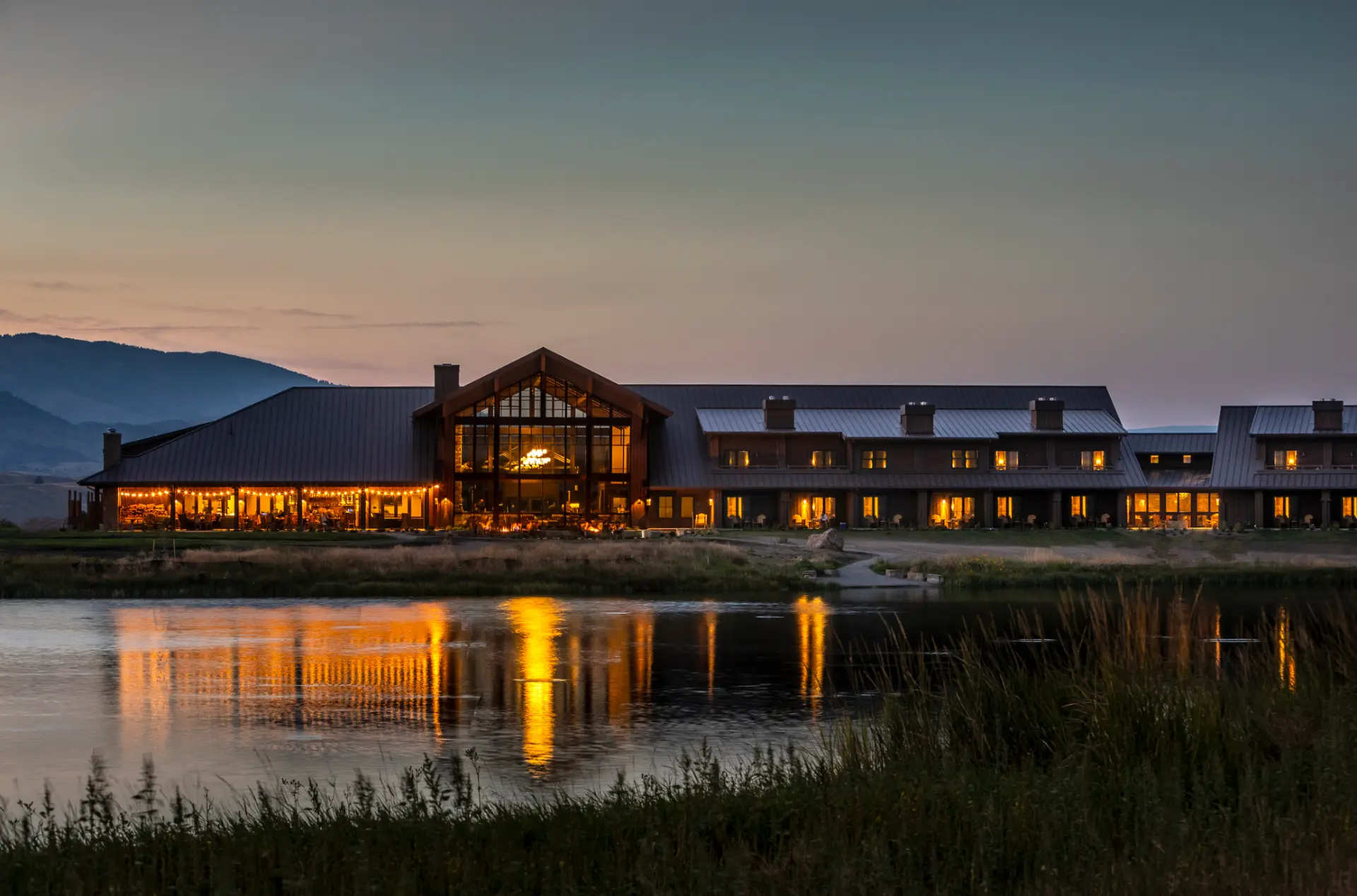 Sage Lodge glowing at dusk beside the pond